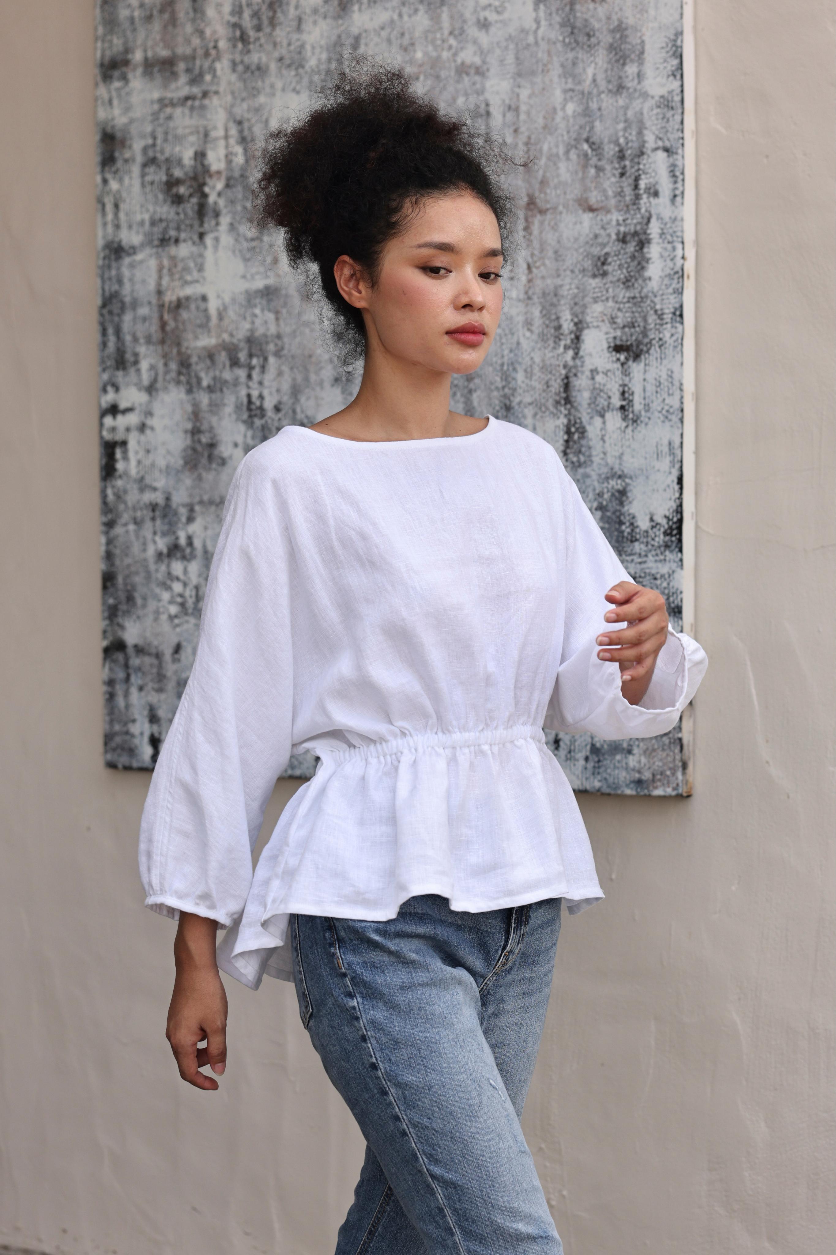 Woman wearing a white blouse and blue jeans against a textured wall.