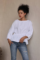 Woman wearing a white blouse and blue jeans against a beige wall