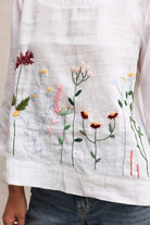 Embroidered floral patterns on a white fabric with a person wearing jeans.