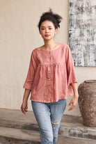 Woman wearing a pink blouse and blue jeans standing in a room with a textured wall and large vase.