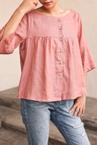 Person wearing a pink blouse with button details and blue jeans on a neutral background