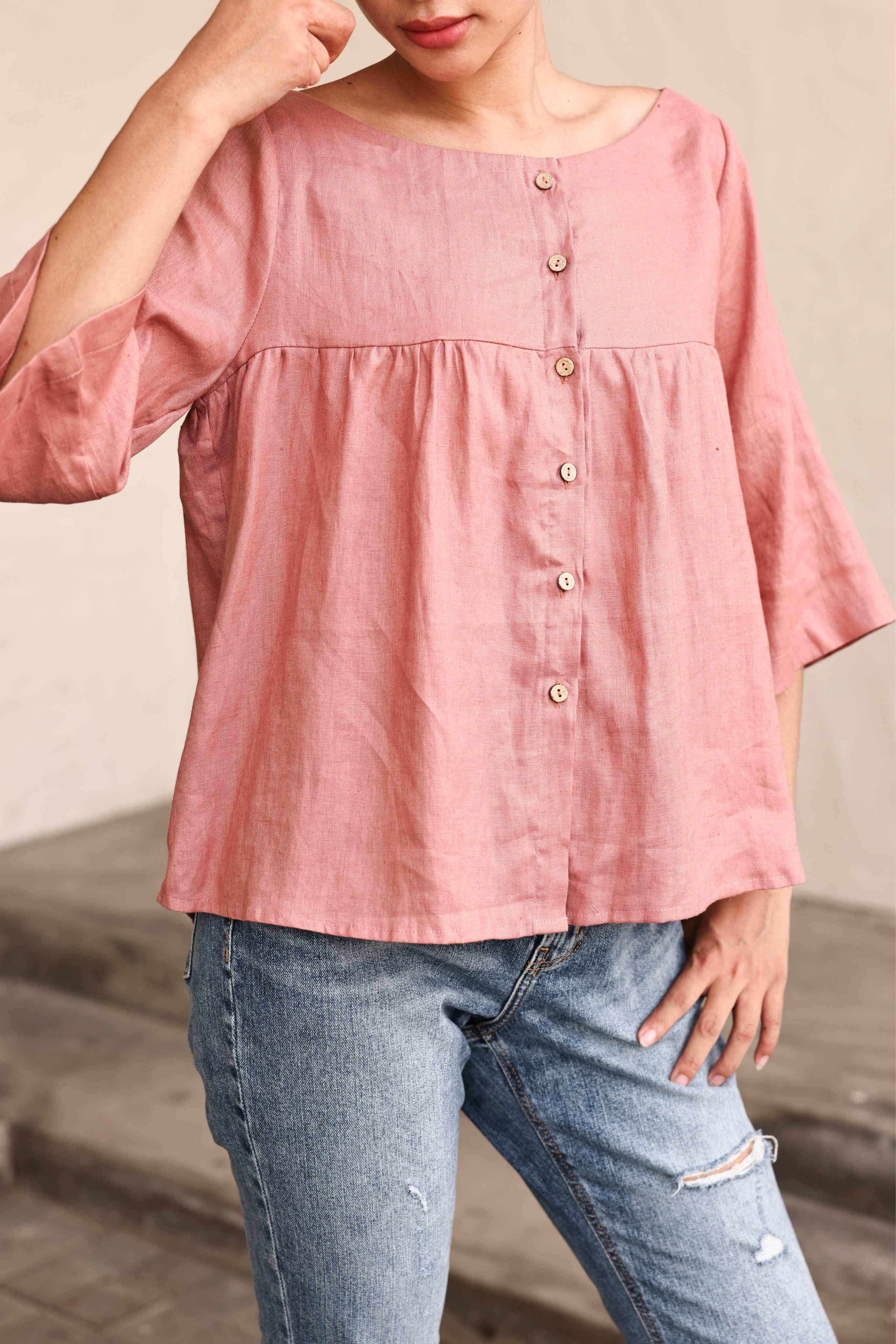 Person wearing a pink blouse with button details and blue jeans on a neutral background