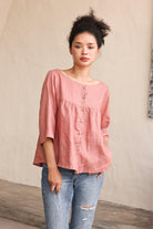 Woman wearing a pink blouse and blue jeans against a beige wall.