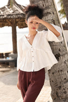 Woman in a white blouse and maroon pants leaning against a tree