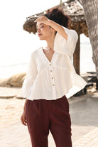 Woman wearing a white blouse and maroon pants standing outdoors near a tree