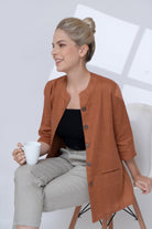 Woman in a brown jacket holding a white mug against a light background