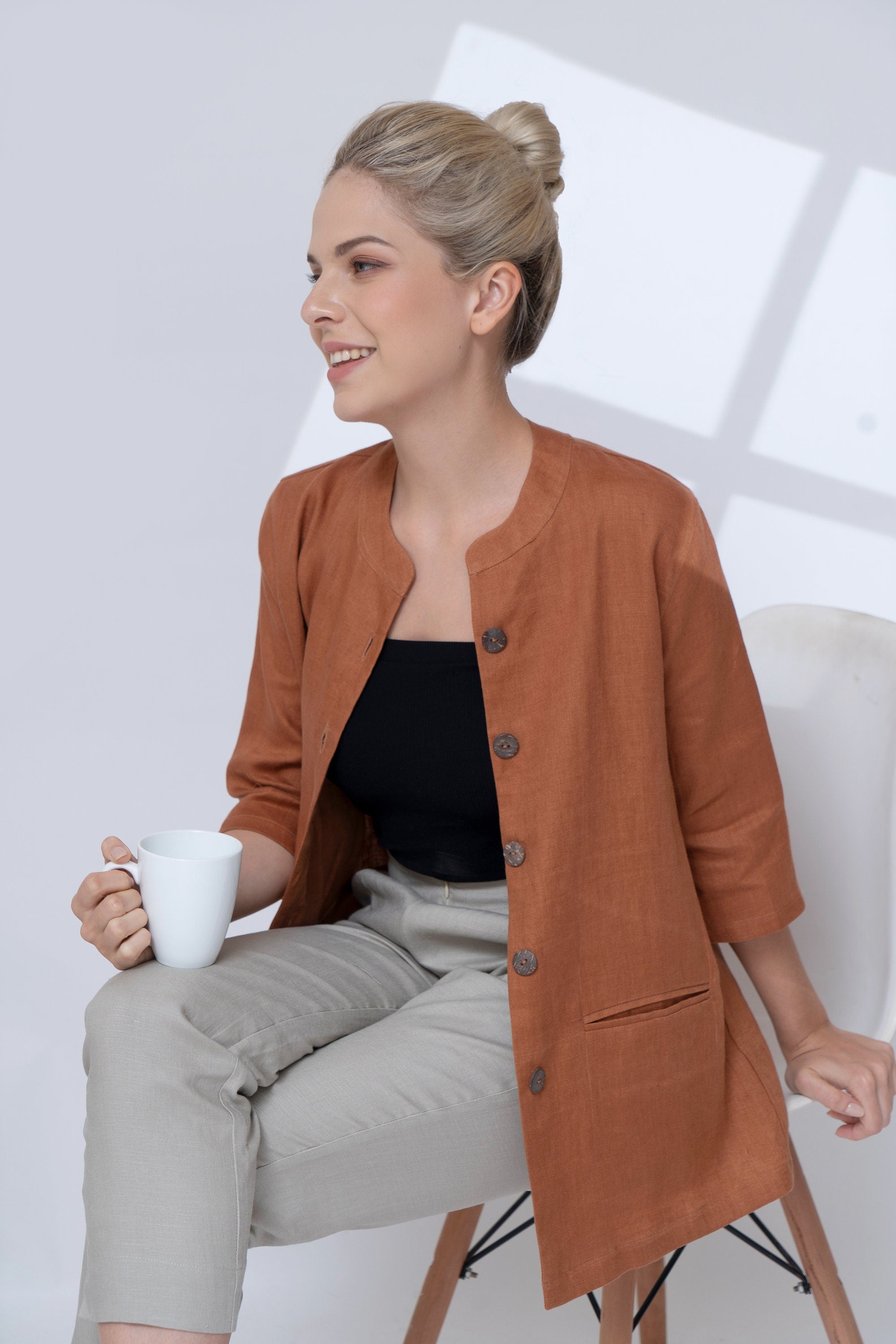 Woman in a brown jacket holding a white mug against a light background