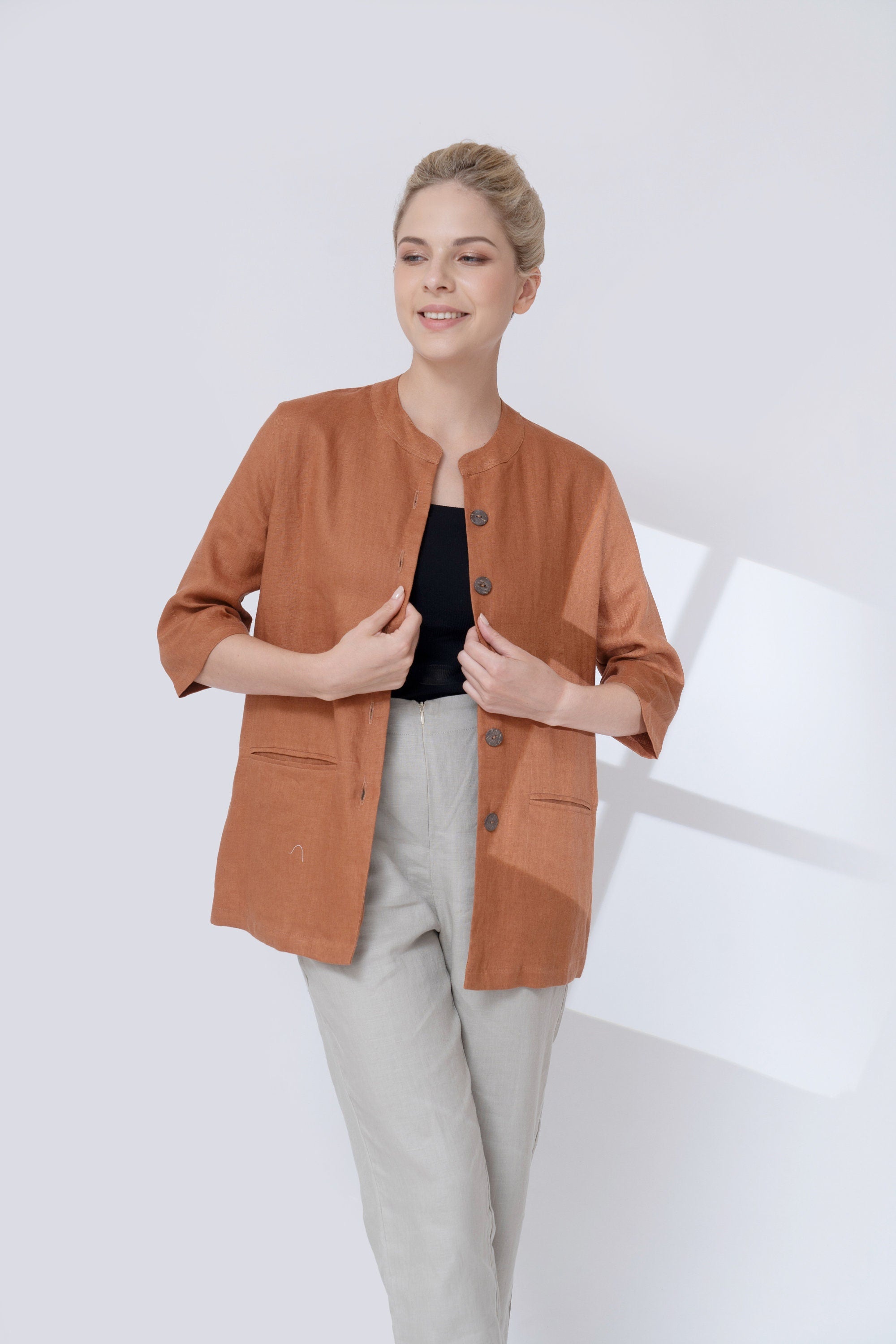 Woman wearing a brown jacket over a black top and light gray pants on a white background