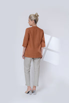 Woman wearing a brown jacket and light gray pants on a white background