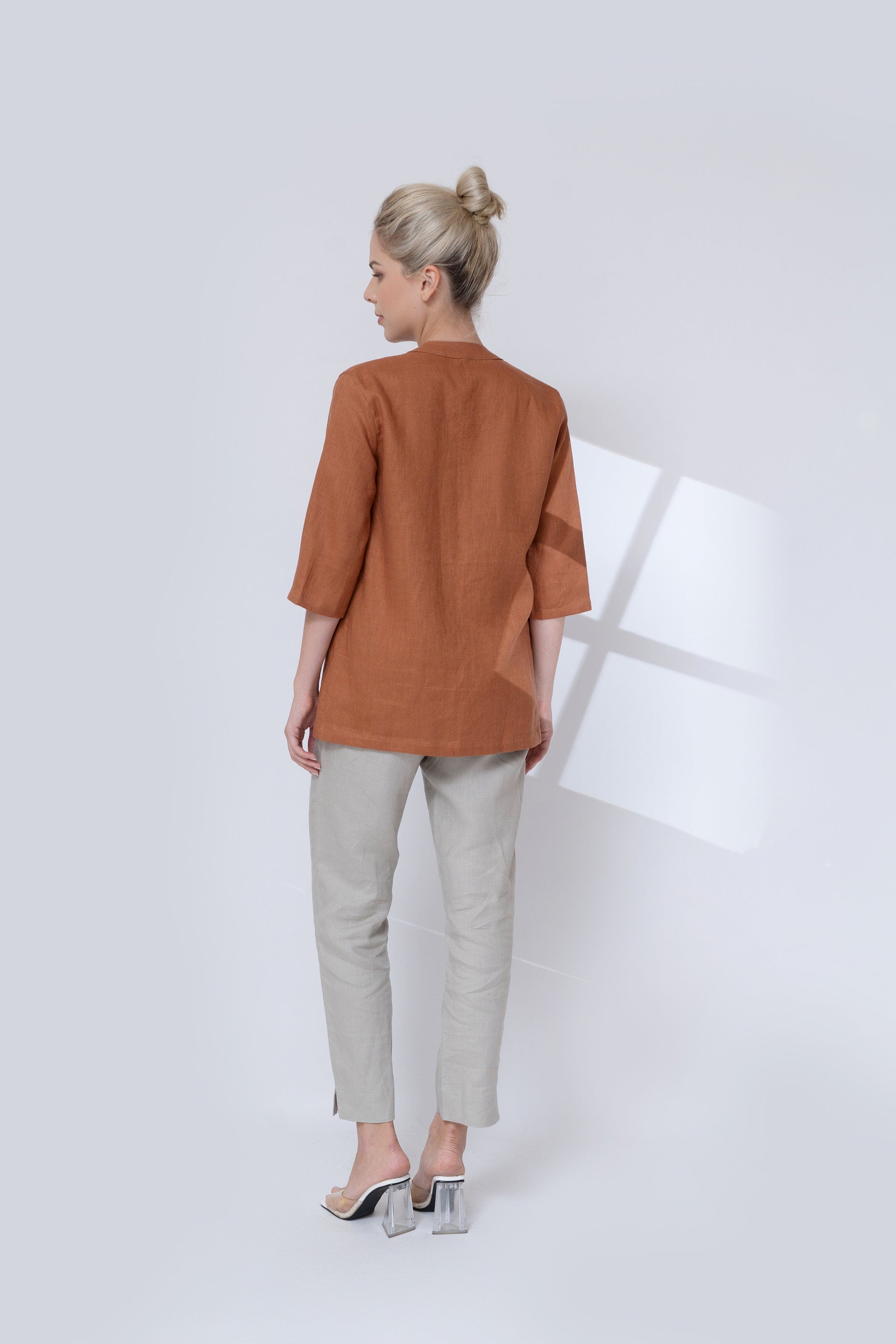 Woman wearing a brown jacket and light gray pants on a white background