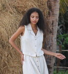 Woman wearing a sleeveless top and skirt standing against a natural background with hay and a tree.