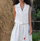 Woman wearing a sleeveless top and skirt with a floral detail, standing outdoors.