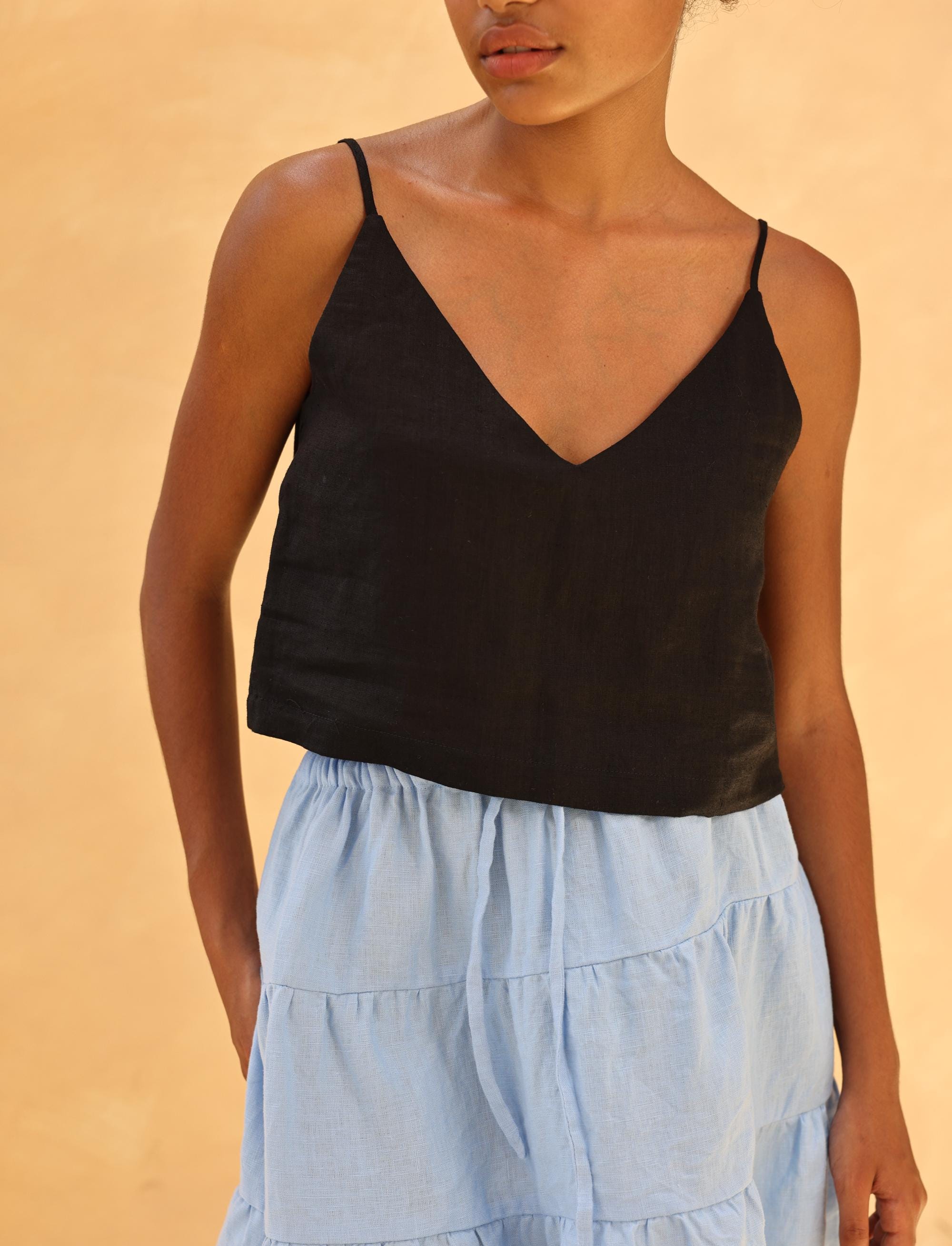 Person wearing a black camisole and light blue tiered skirt against a beige background