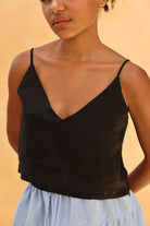 Woman wearing a black spaghetti strap top against a beige background