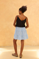 Woman wearing a black top and light blue skirt against a beige background