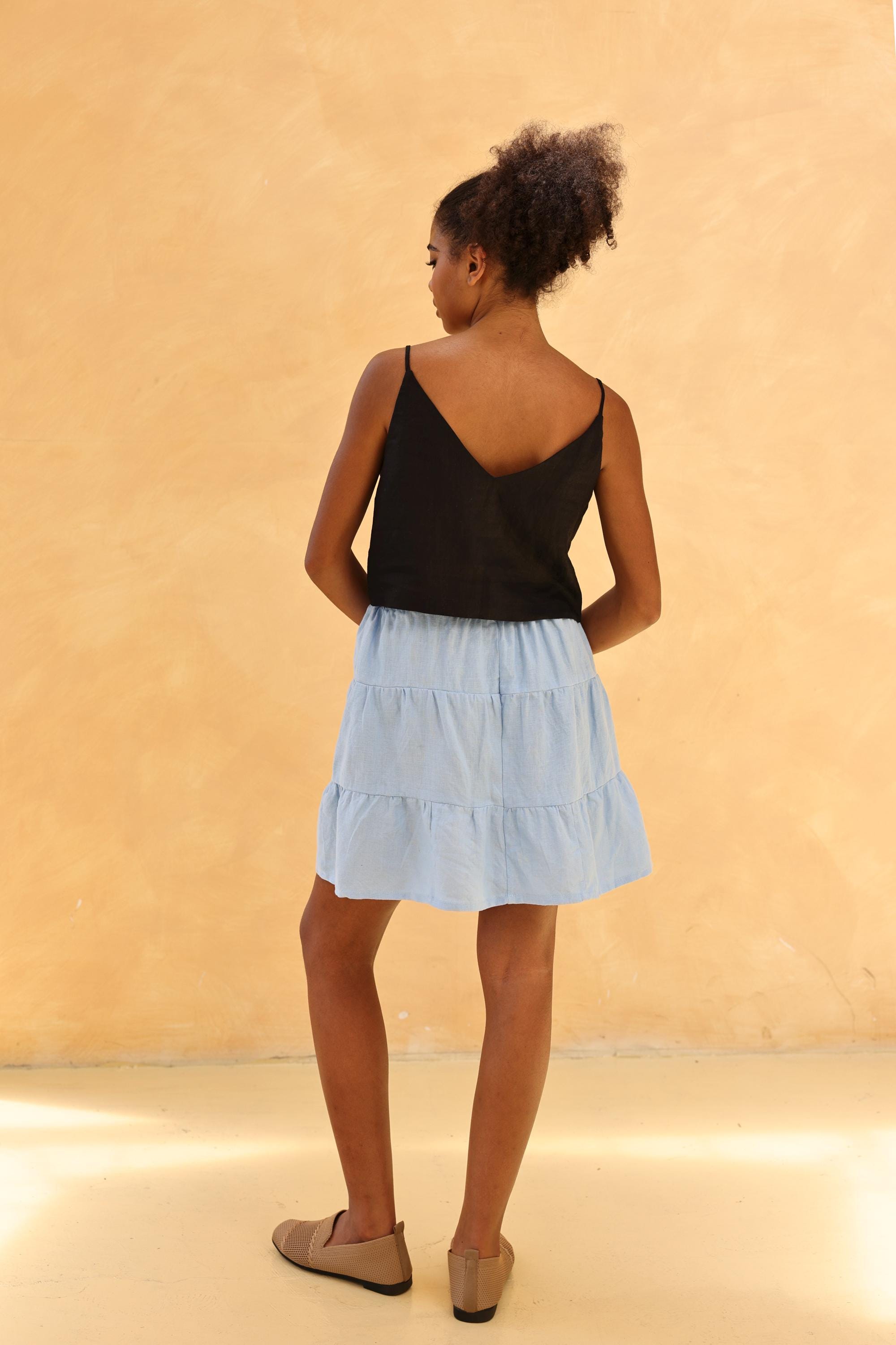 Woman wearing a black top and light blue skirt against a beige background