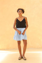 Woman wearing a black tank top and light blue skirt against a beige background