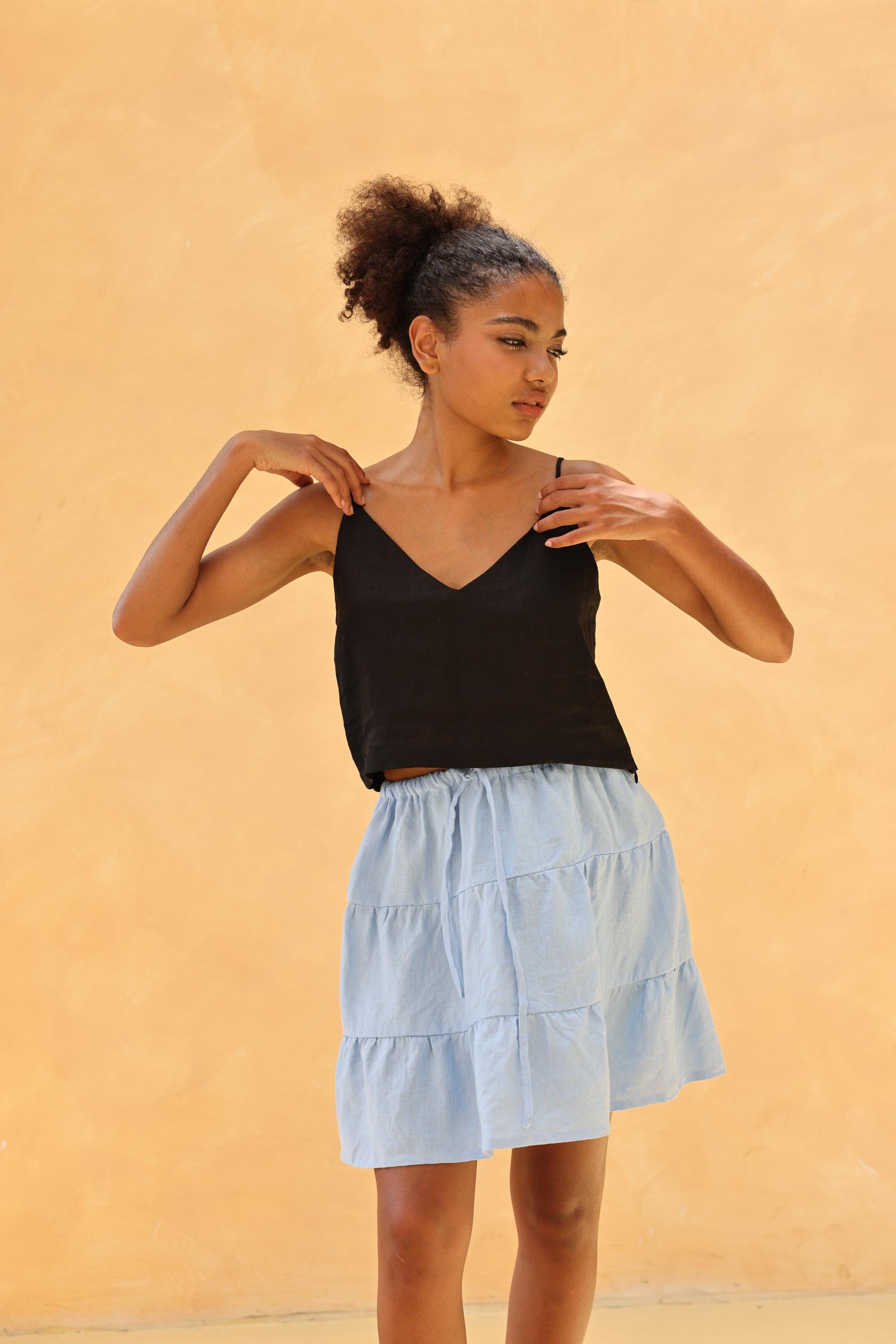 Woman wearing a black top and light blue tiered skirt against a beige background