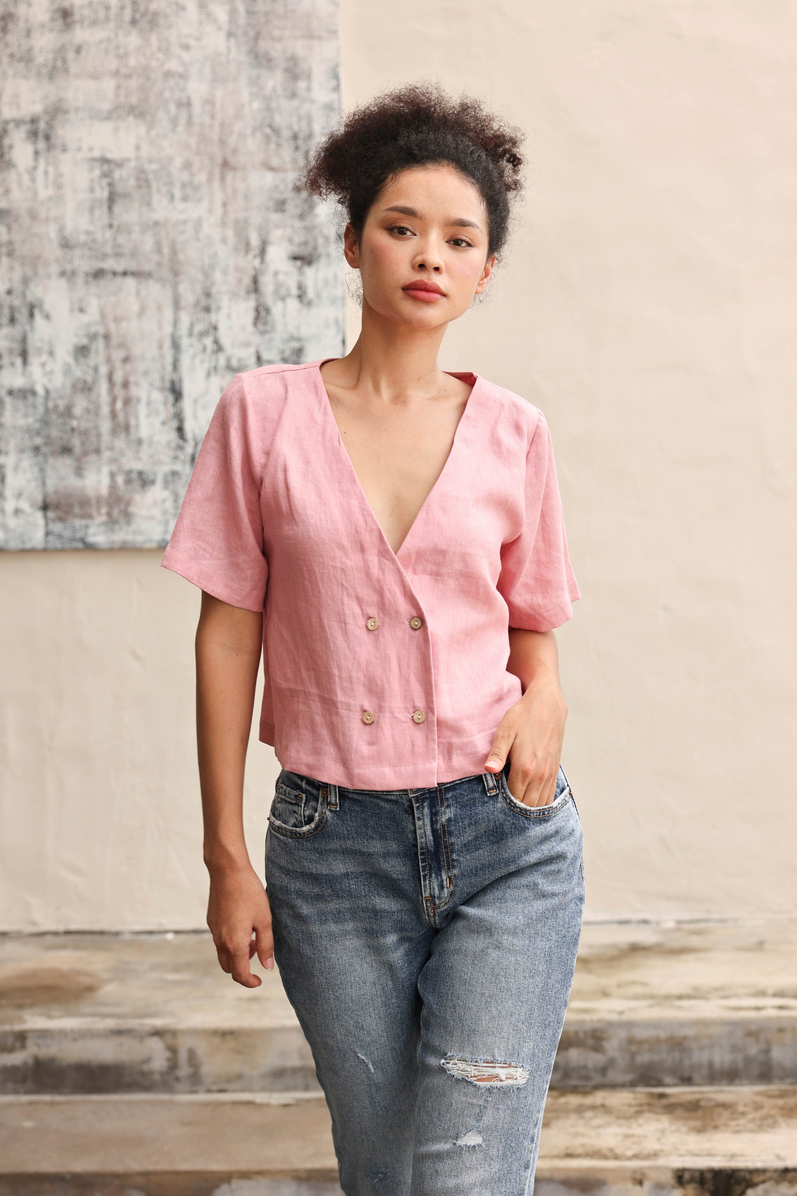 Woman wearing a pink blouse and blue jeans against a neutral background
