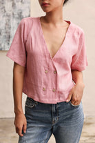 Person wearing a pink blouse with short sleeves and blue jeans against a neutral background
