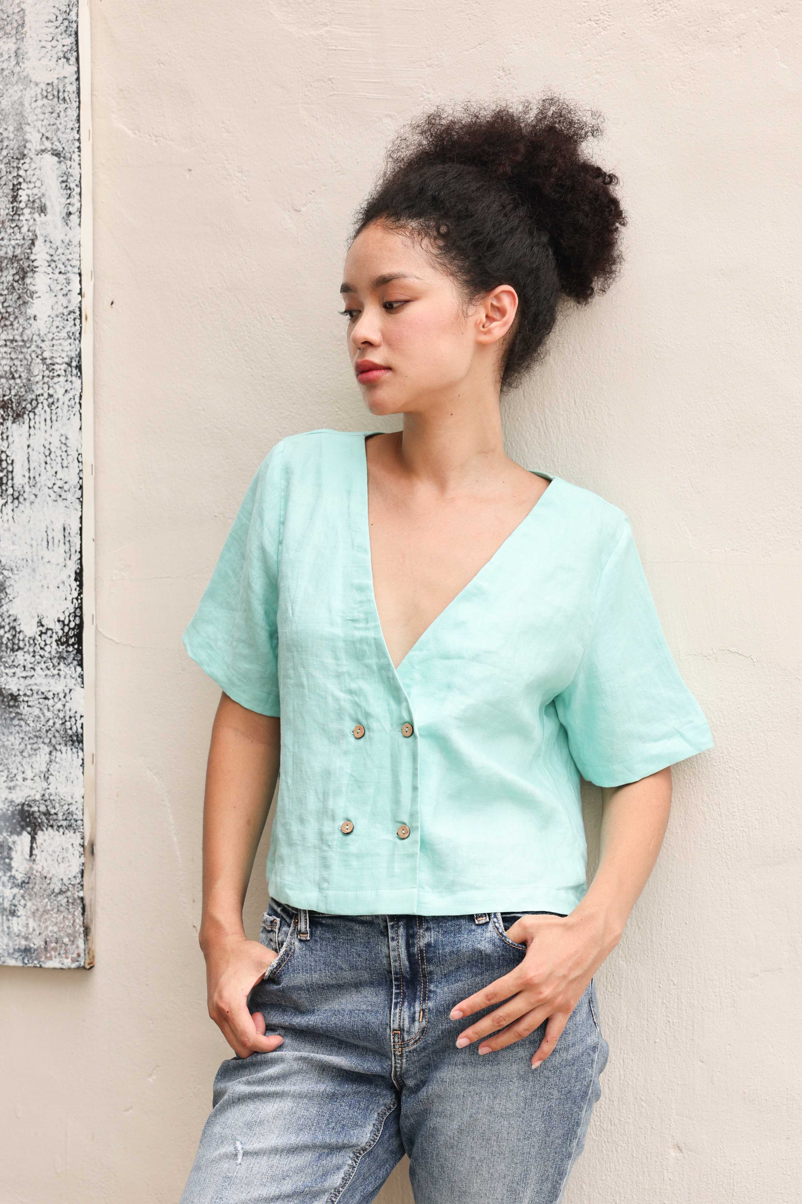 Woman wearing a light blue top and jeans against a beige wall.