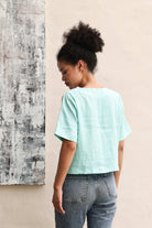 Person wearing a light blue top and jeans against a beige wall with abstract art.