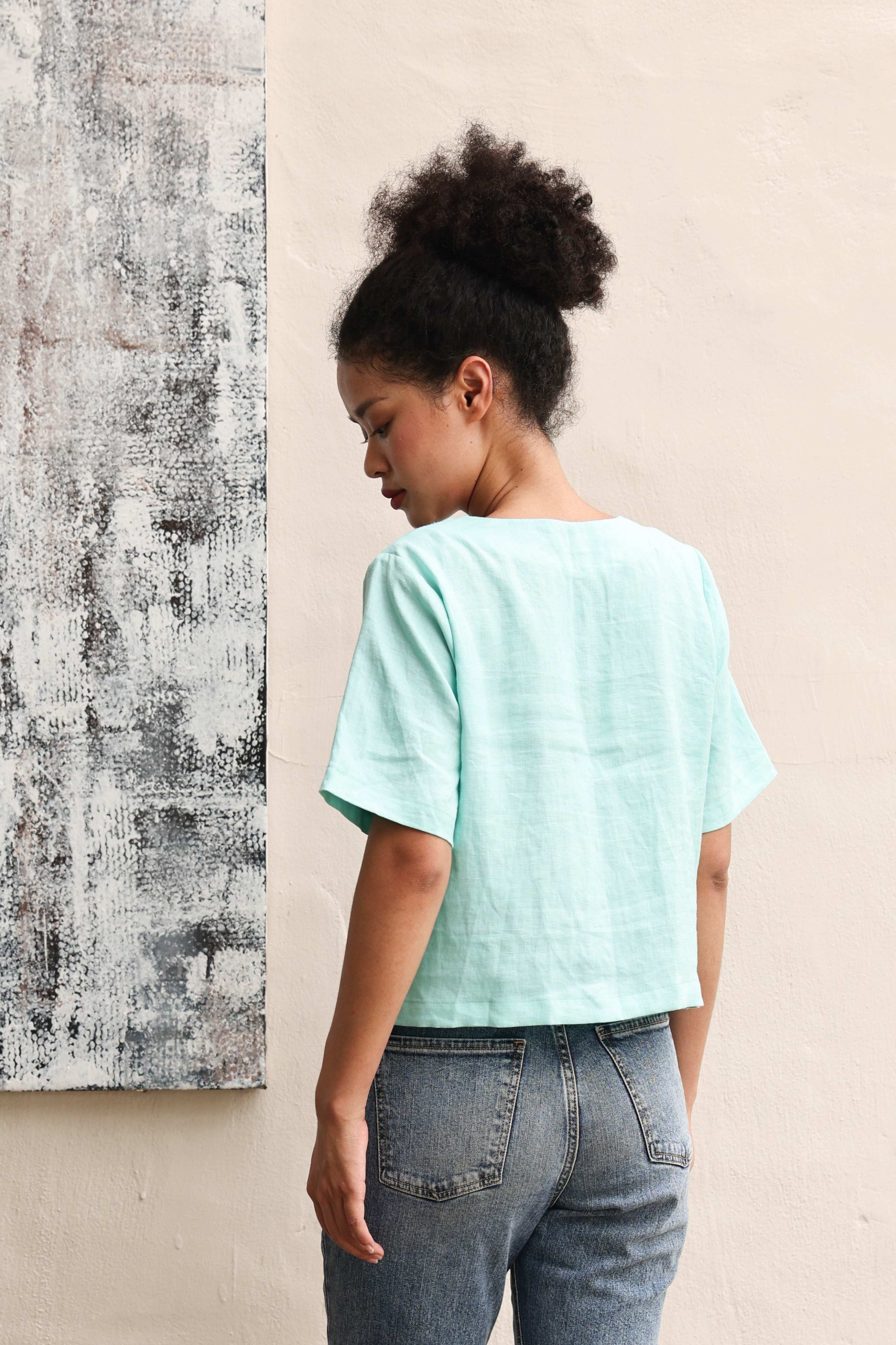 Person wearing a light blue top and jeans against a beige wall with abstract art.
