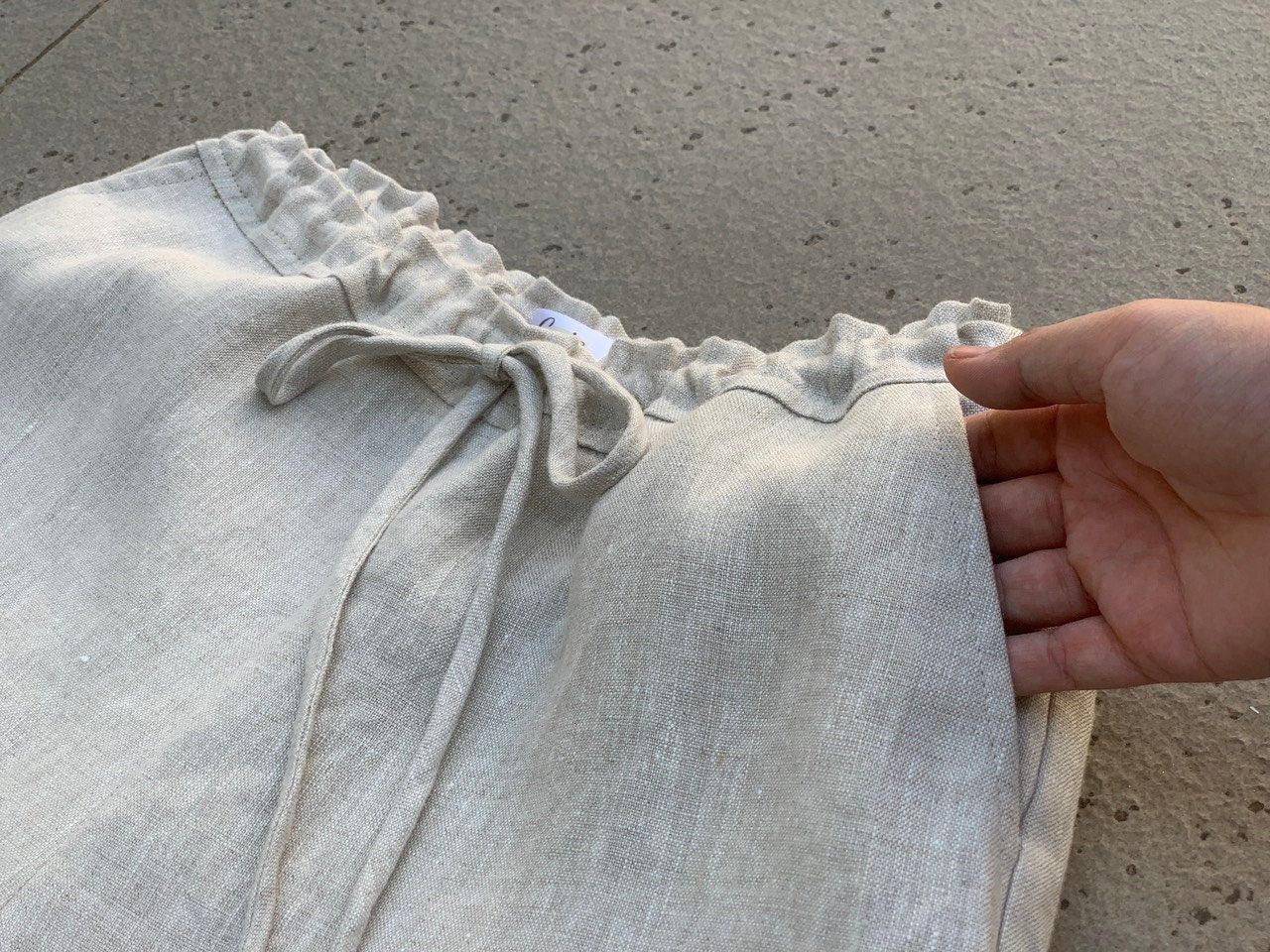 Light gray pants with drawstring waist held by a hand on a concrete surface