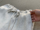 Light gray pants with drawstring waist held by a hand on a concrete surface