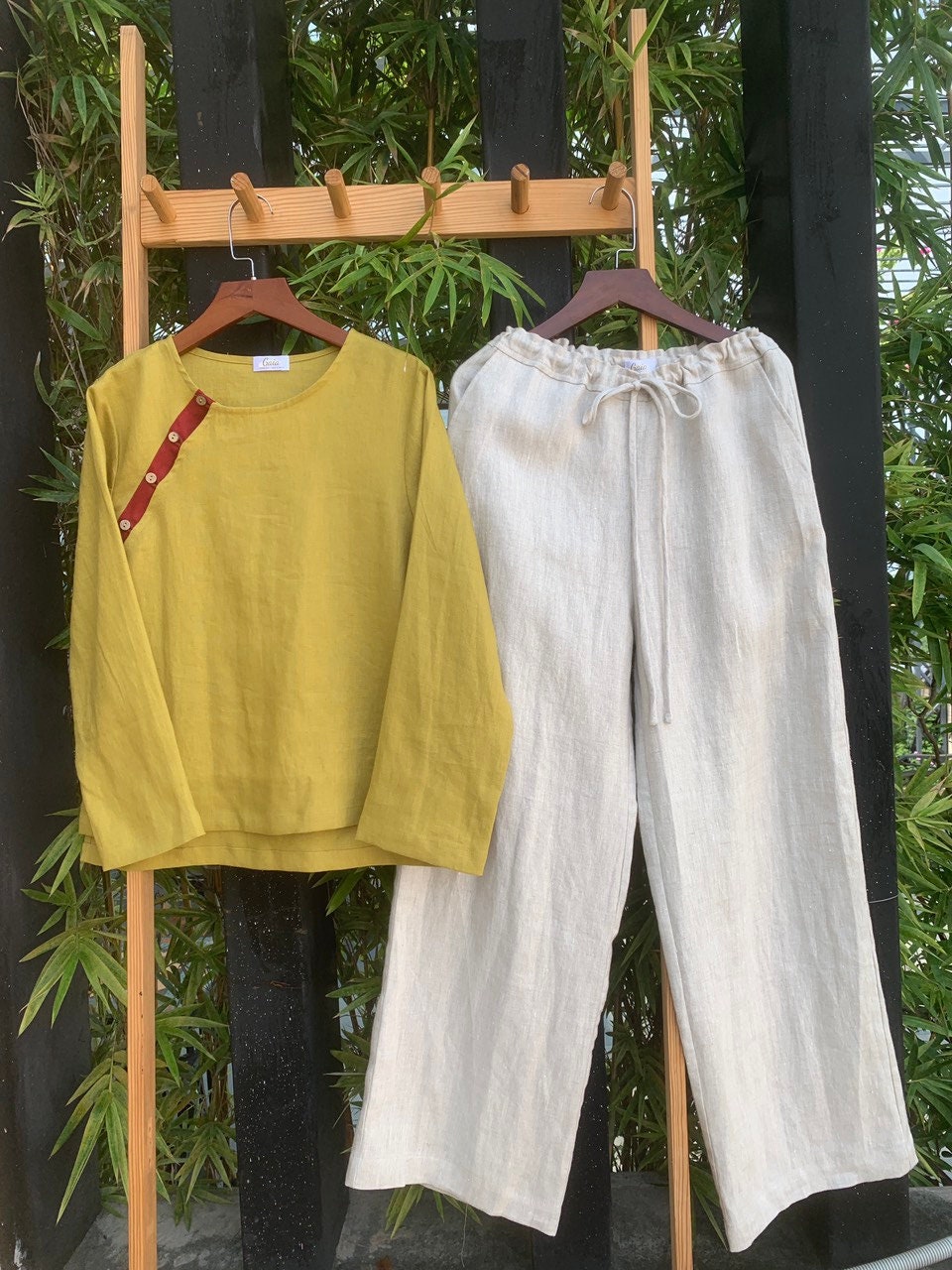 Yellow top and pants hanging on a wooden rack against a natural background.