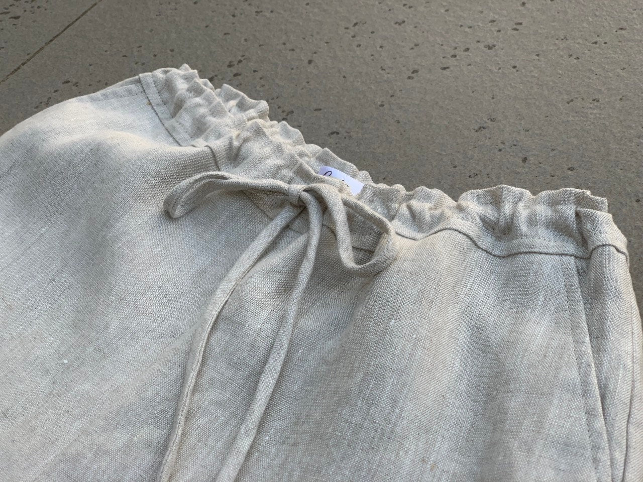 Light gray linen top with drawstring on a concrete surface