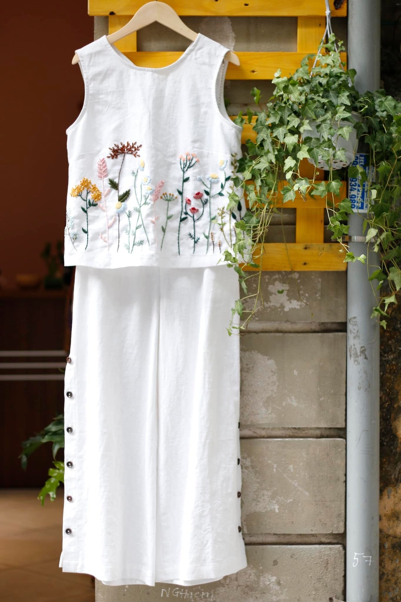 White sleeveless top with floral embroidery on a wooden hanger against a rustic background.