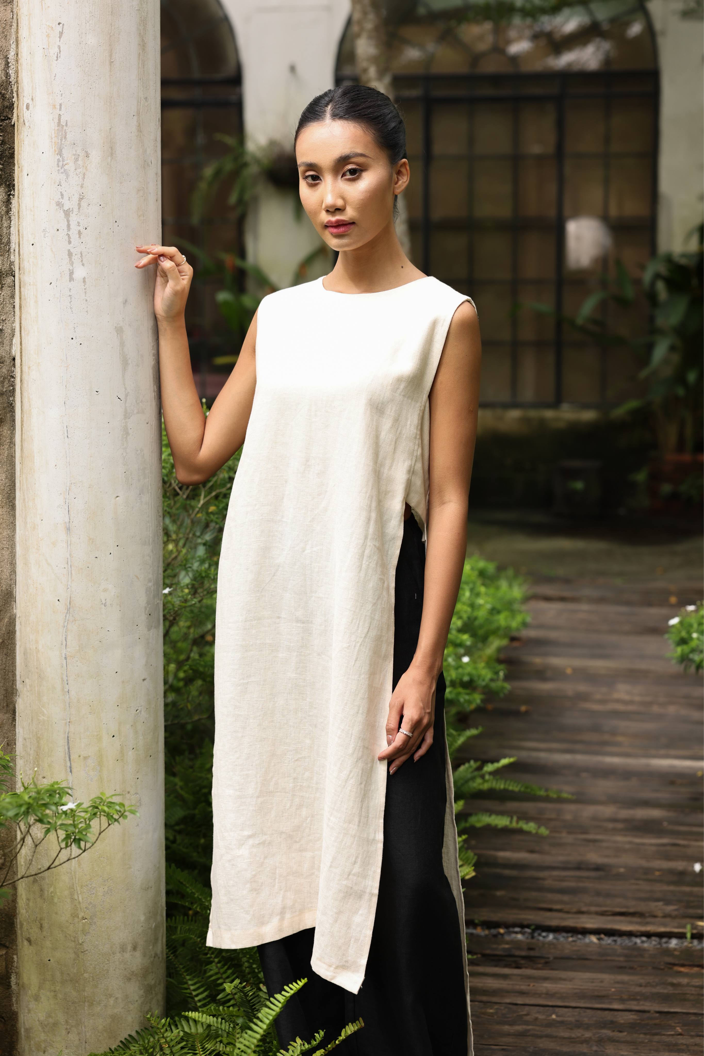 Woman wearing a long, light-colored dress standing outdoors near a column.