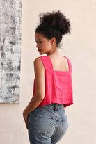 Woman wearing a pink sleeveless top and blue jeans against a textured wall.