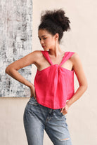 Woman wearing a bright pink top and jeans against a textured wall.