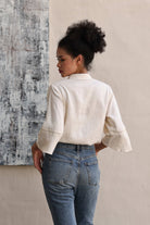 Woman wearing a beige blouse and blue jeans standing against a textured wall.