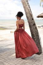 Woman in a red skirt standing by a palm tree on a beach.