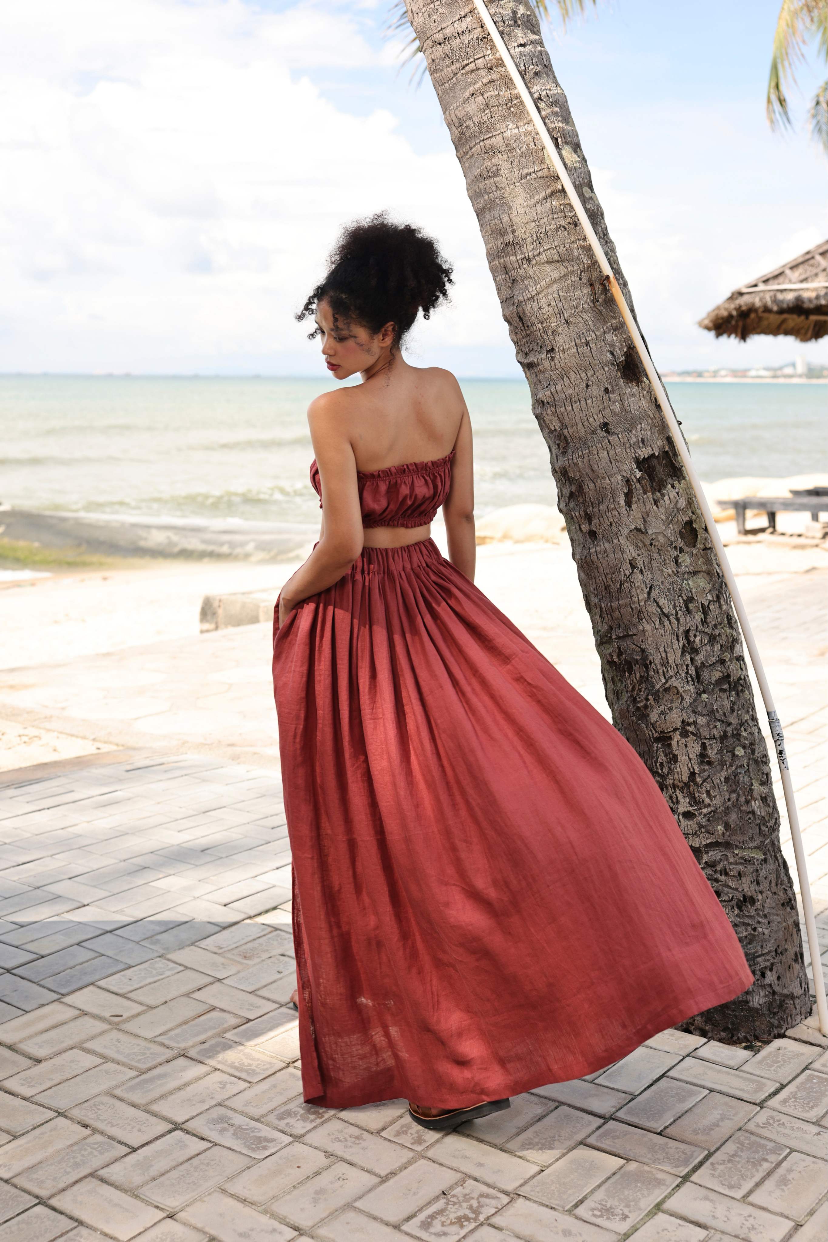 Woman in a red skirt standing by a palm tree on a beach.