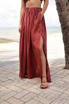 Person wearing a long rust-colored skirt with a slit on a paved walkway.