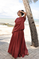 Woman in a red outfit standing by a palm tree on a beach.