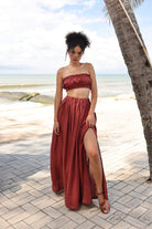 Woman in a red strapless top and long skirt standing on a beach path with palm trees.