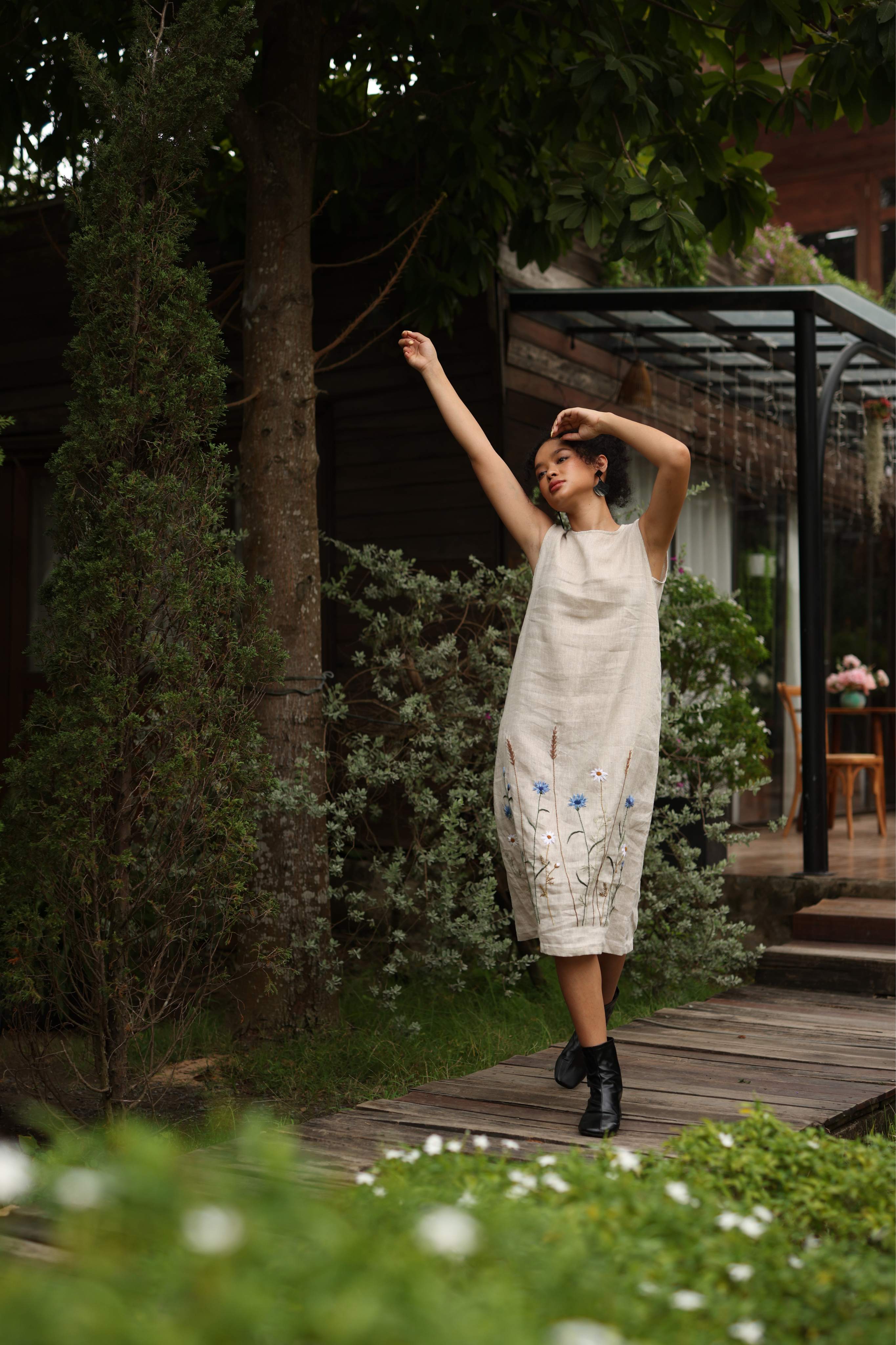 Woman in a dress standing on a wooden path with greenery around