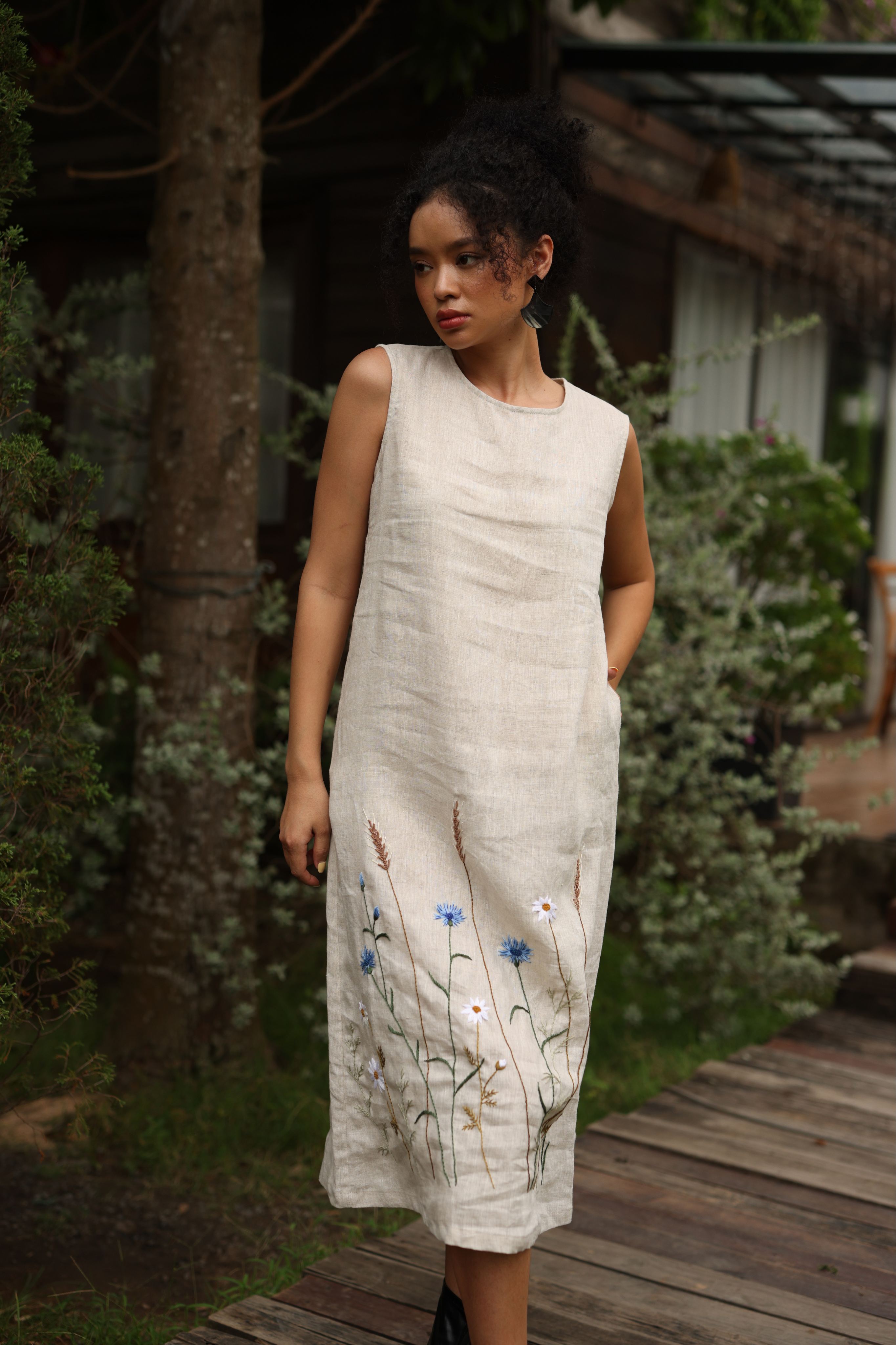 Woman wearing a light-colored dress with floral embroidery in an outdoor setting