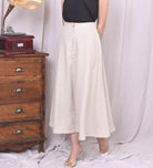 Person wearing a white skirt standing next to an old wooden dresser with a record player.