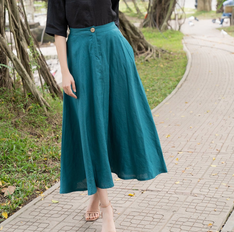 Person wearing a teal skirt and black top on a paved path with greenery.