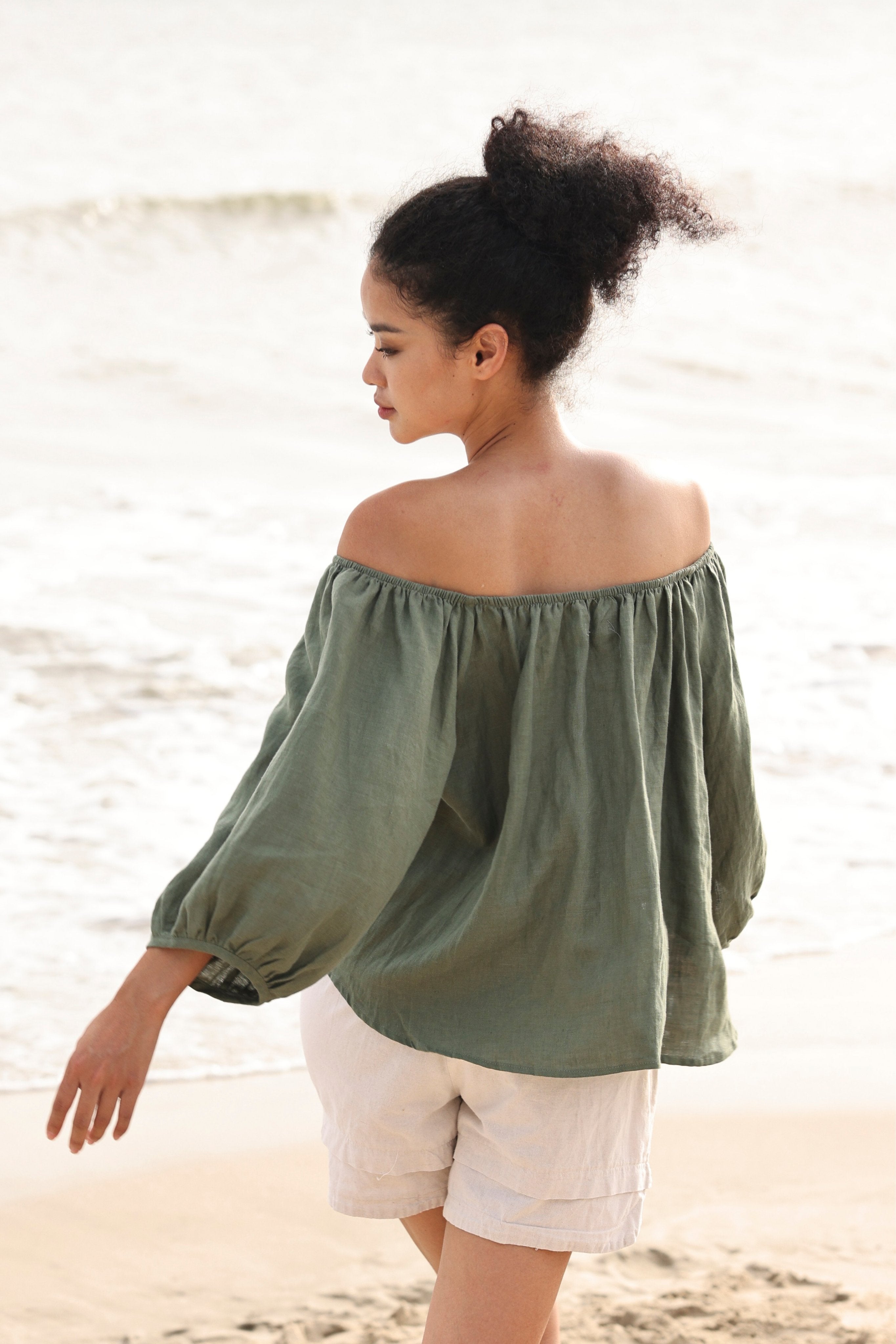 Woman wearing a green off-shoulder top and white shorts on a beach.