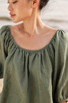 Woman wearing a green blouse with puffed sleeves against a blurred background