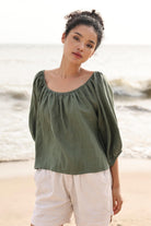 Woman wearing a green top and white pants standing on a beach.