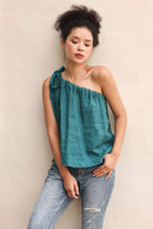 Woman wearing a teal one-shoulder top and jeans against a beige background