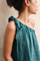 Woman wearing a teal one-shoulder top against a neutral background